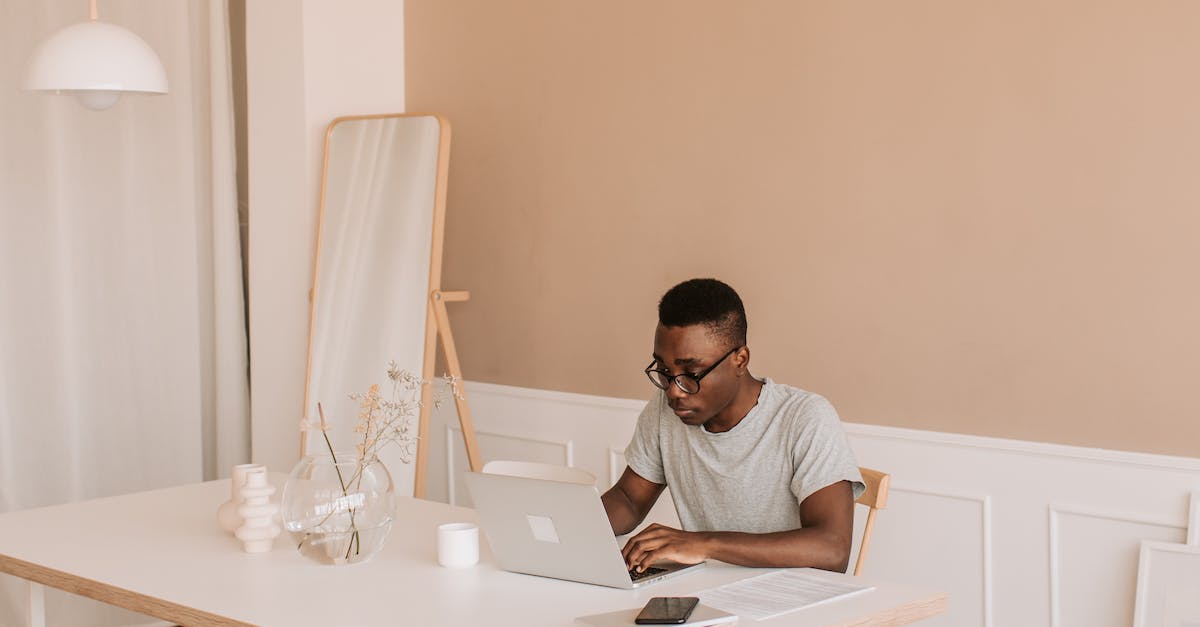 Man Focused On Laptop Screen Working At A Minimalist Desk In A Modern Home Office Environment, Emphasizing Online Privacy And Technology.