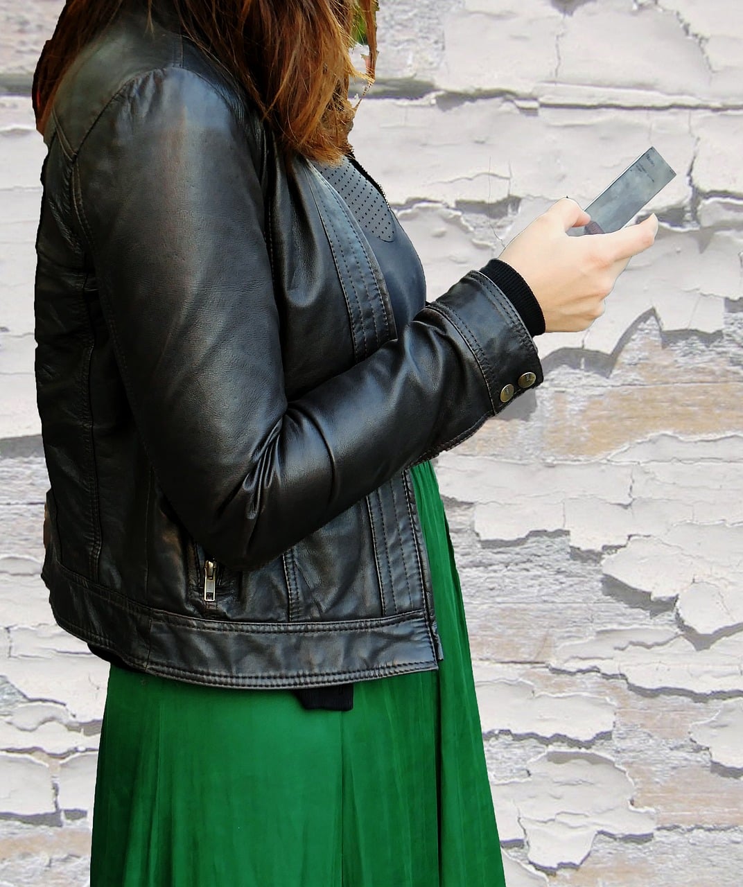 Woman In A Black Leather Jacket And Green Dress Using A Smartphone, Representing Digital Communication For Social Network Ads Analysis.