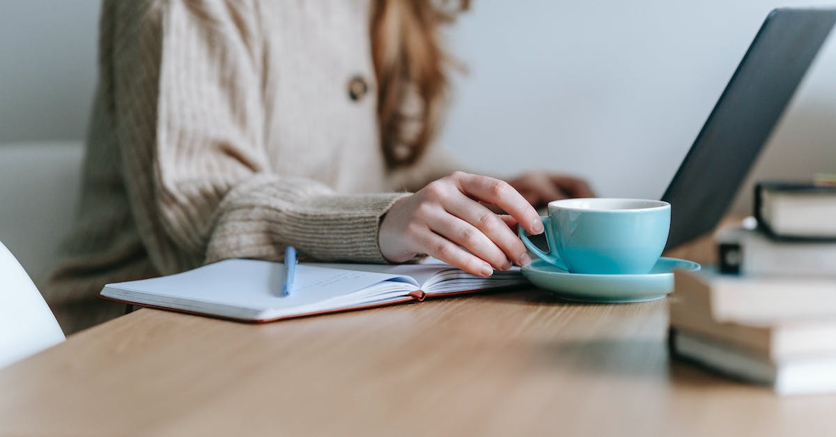 Person in a beige sweater sitting at a wooden desk with a laptop, a notebook, and a blue cup, symbolizing 2025 digital marketing trends and maximizing ad and campaign success.